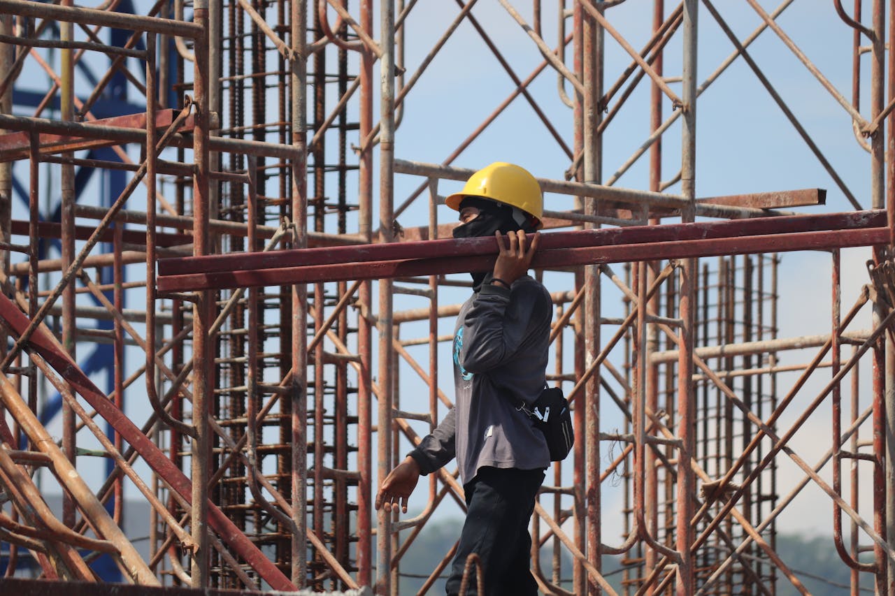 Mastering the First Impression: Your intriguing post title goes here A construction worker with safety gear carrying a metal beam amidst scaffolding at a busy construction site.